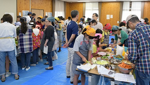 みのり館の広間で野菜を切ってカレーを作る参加者たち