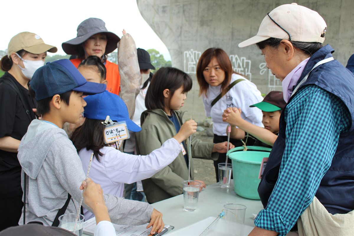 橋の下の広場で、試験管を使って川の水を調べる子どもたち