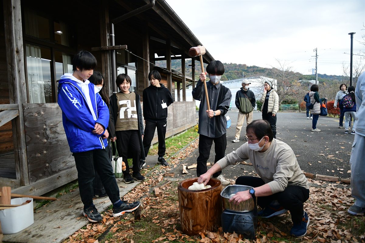 臼と杵でもちをつく様子。まわりで順番を待つ子どもたち